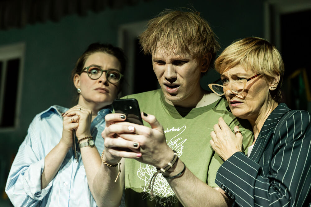 Drei Personen stehen eng zusammen und blicken gemeinsam auf ein Smartphone. Zwei von ihnen sehen erschrocken aus, während die dritte Person irritiert schaut.